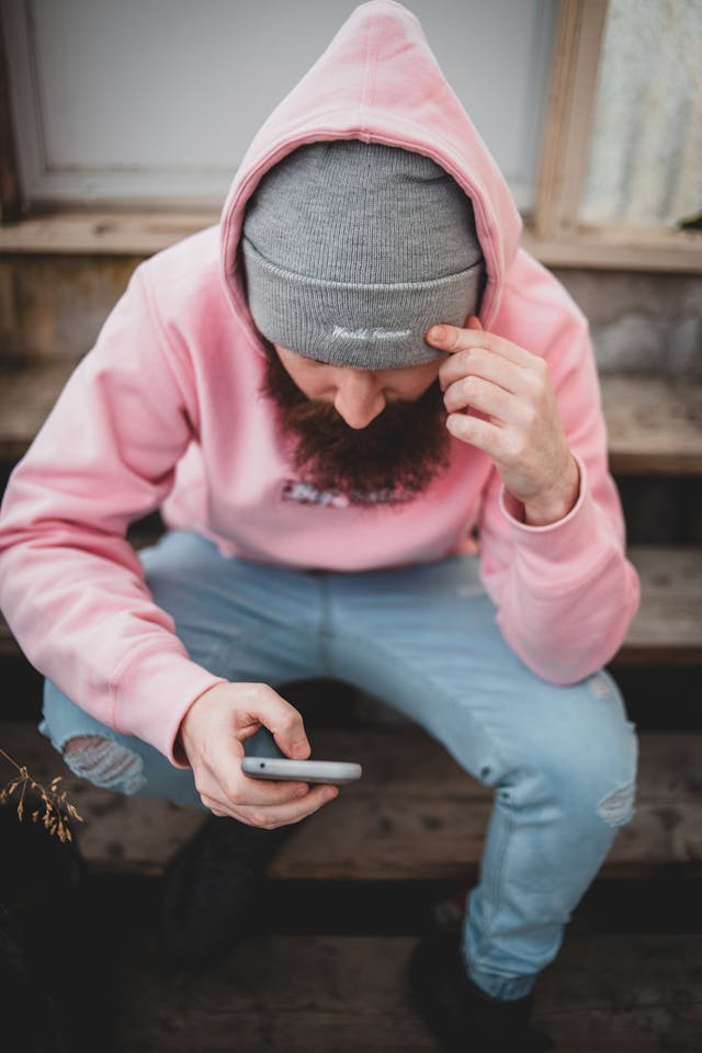A man in a pink sweater looks down at his phone.