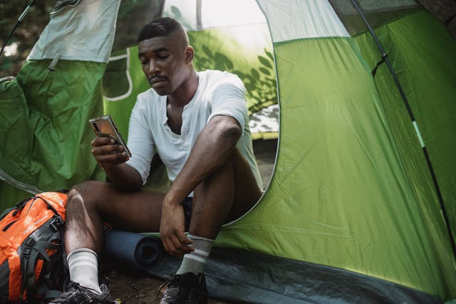 A man sitting in a tent uses his phone.