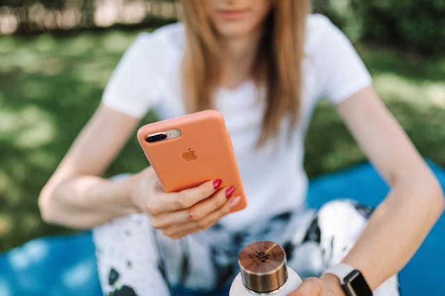 A woman holds a phone with a coral case.