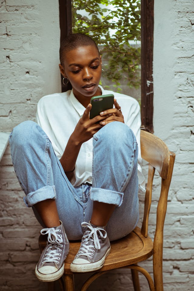 A woman sits on a chair and uses a phone.