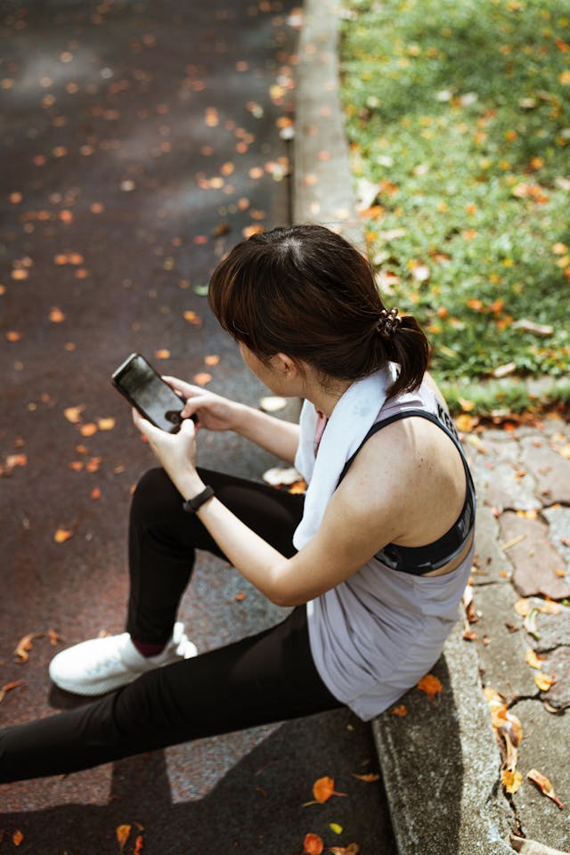 A woman in exercise clothes uses a phone on the sidewalk.