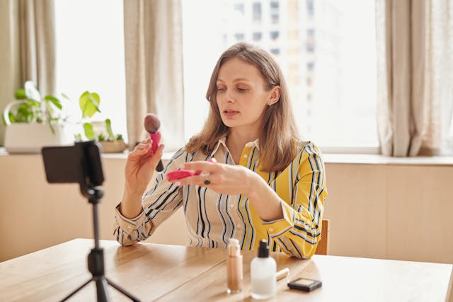 A woman films a makeup tutorial in front of a camera phone.