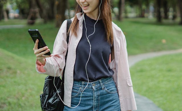 A woman grins as she uses her cell phone with headphones.
