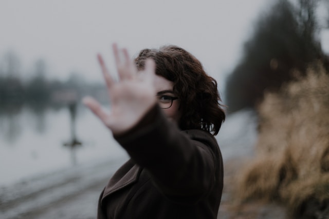 A woman wearing glasses blocks half of her face with her hand.