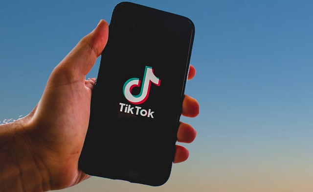 Someone holds a phone showing the TikTok logo on the screen.