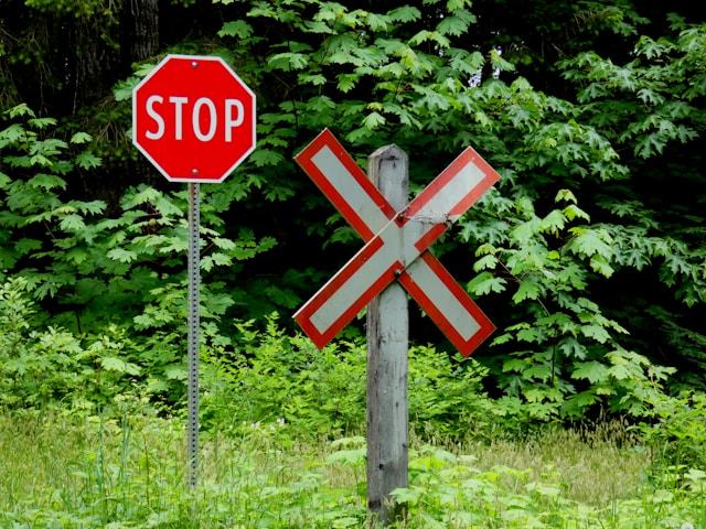 A red and white Stop sign stands beside a red and white X sign on a wooden pole.