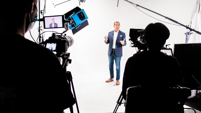 A man stands against a white background and in front of multiple cameras for a live broadcast.