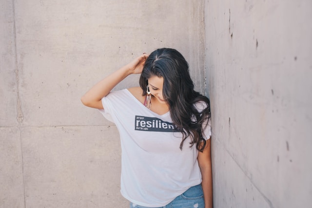 A woman in a white shirt looks down as she smiles and covers half of her face with her long hair.