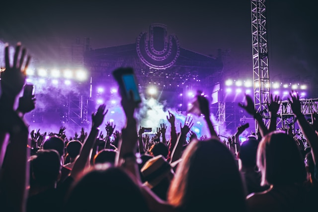A big audience raises their hands as they watch artists performing on a stage.