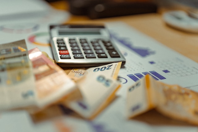 A pile of paper currency and a calculator sit on top of printed graphs.