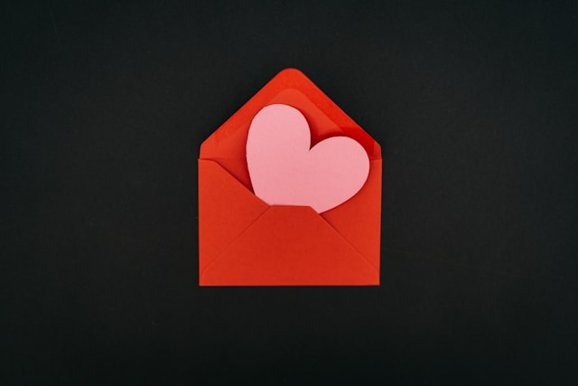 A pink paper heart inside a red envelope.