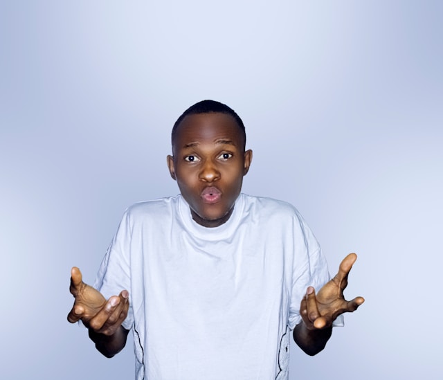 A young man in a white shirt holds out his open hands in a gesture of wonder.