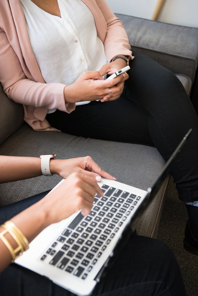 A woman uses her phone next to a person using a laptop.