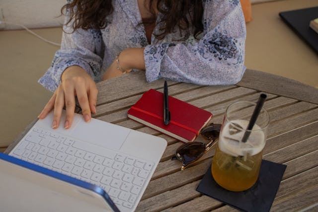 =A woman at a wooden table types on a laptop.