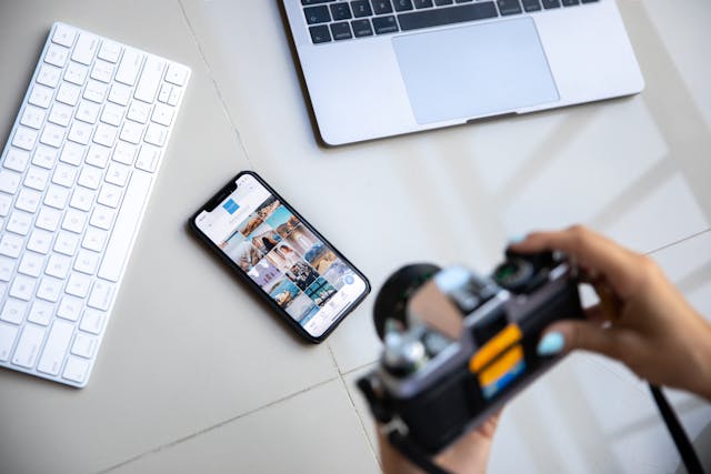 A person with a large camera takes a photo of a phone and keyboard.