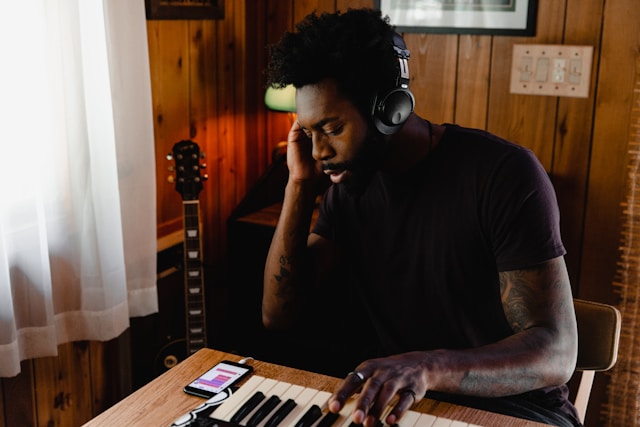 A musician plays notes on a keyboard and listens to the sound through his headphones.