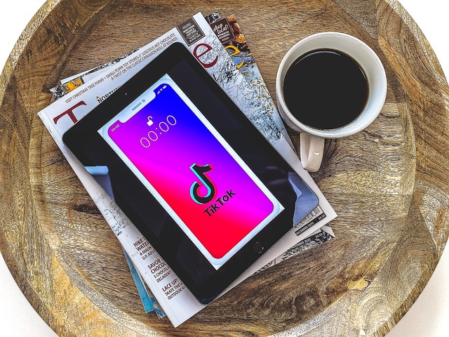 A tablet on a stack of magazines beside a cup of coffee shows the TikTok logo.