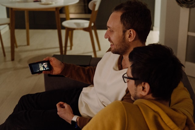 A couple sits on a couch and watches videos on a phone.