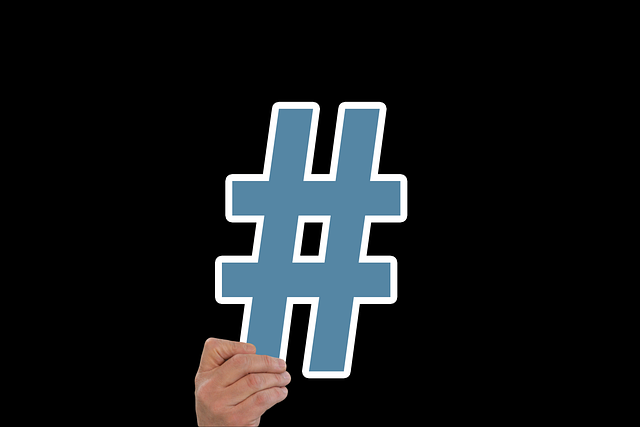 A person holds a giant hashtag on a black background.