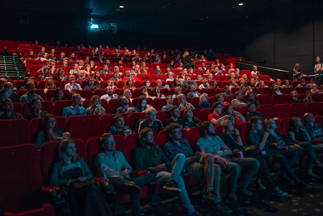 People sit on red chairs in a movie theater.