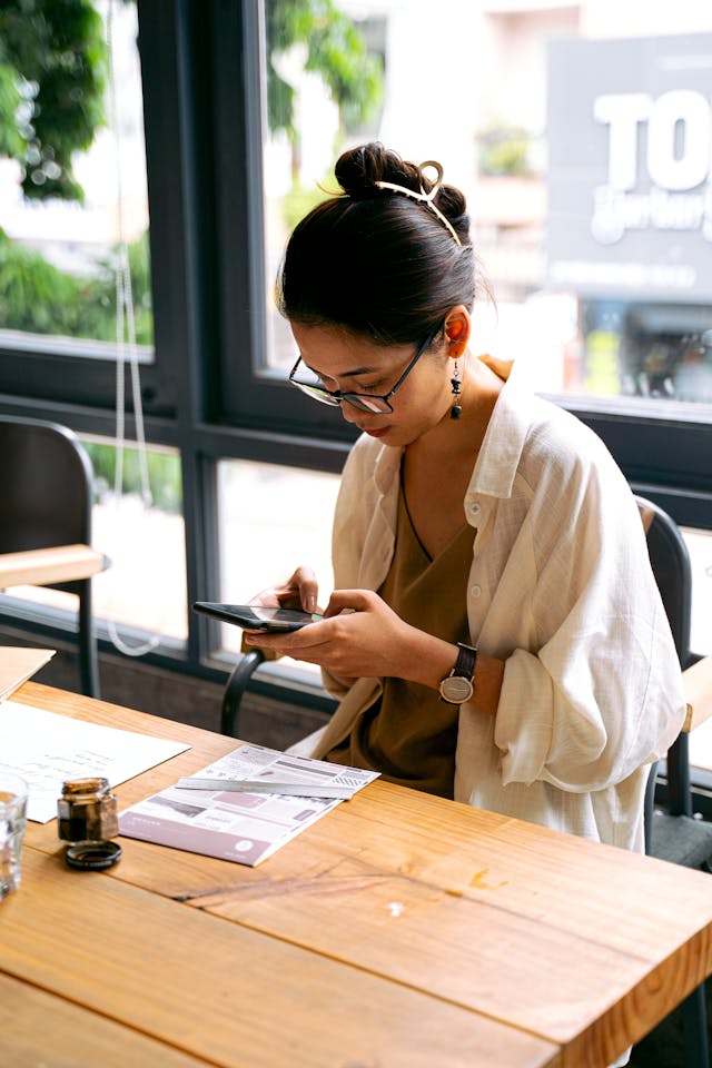 A woman at a wooden table types on her cell phone.