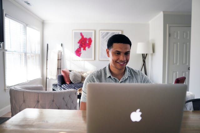 A man types on his laptop while sitting at a table.