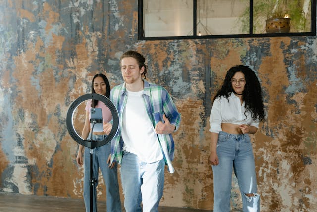 A man taps his phone screen as his two female friends wait in the background.