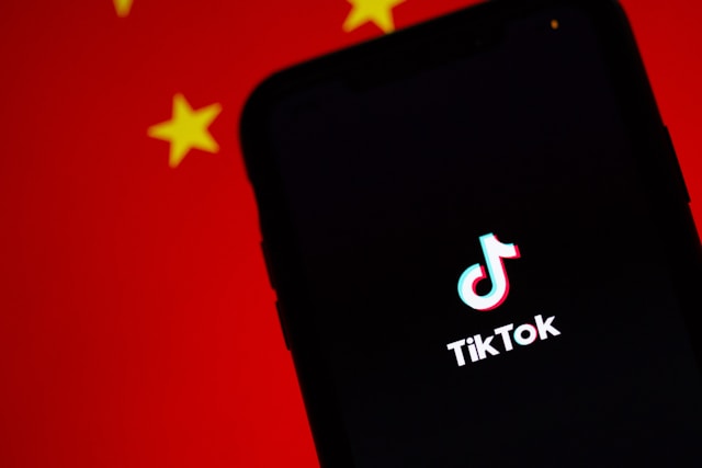 A black phone screen with the TikTok logo is in front of a red flag with yellow stars.