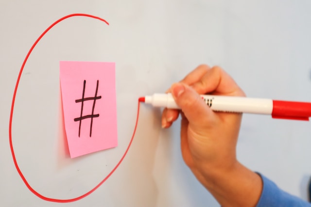 A person draws a circle around a pink sticky note with the hashtag symbol on it.