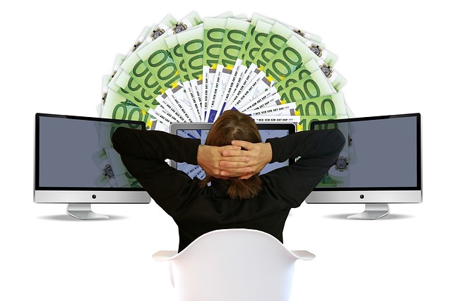 A person sits in front of three computers with notes of cash in front.