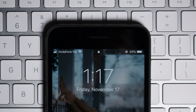 A phone screen showing the time and date sits on top of a laptop keyboard.