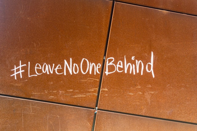 A hashtagged message on a tiled wall reads “#LeaveNoOneBehind.”