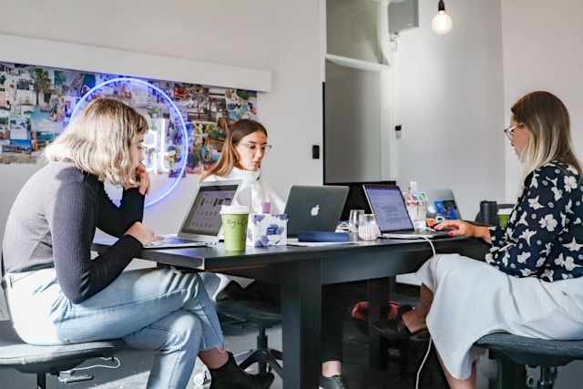 A group of social media marketers sit around a table and work on their laptops.